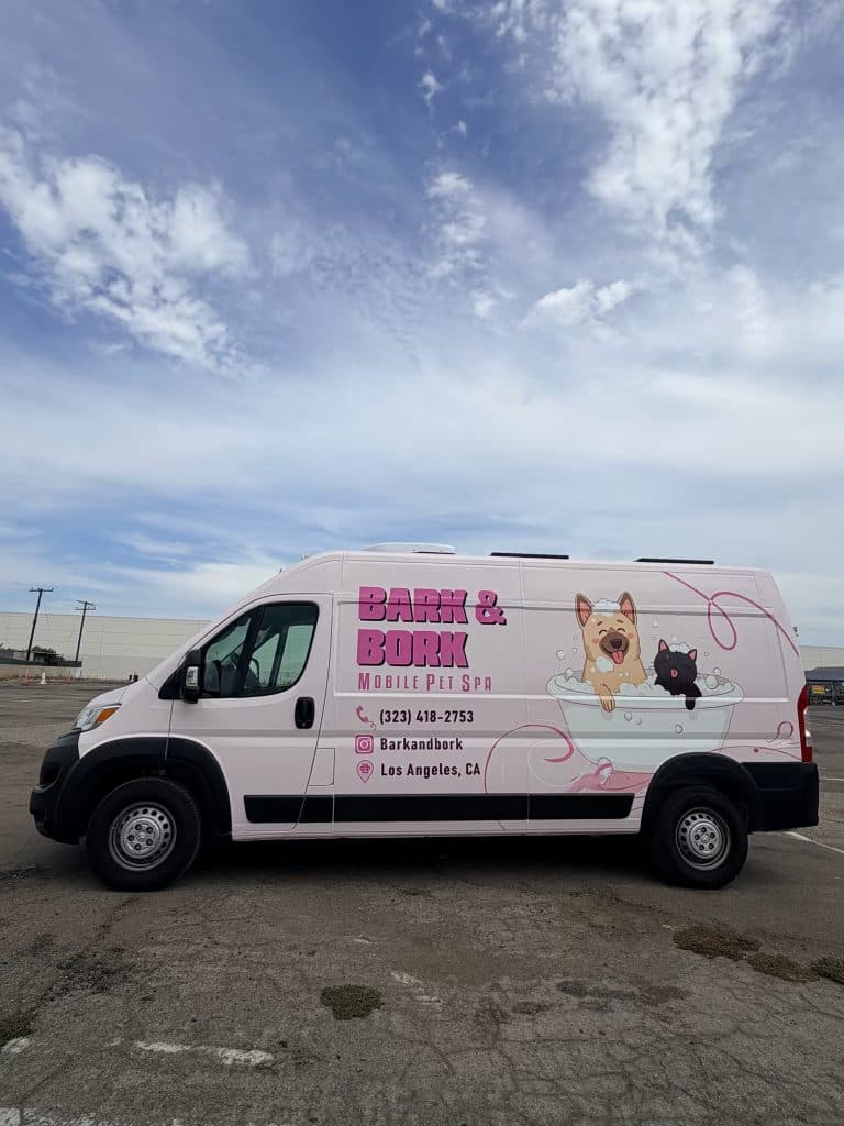 The Bark and Bork mobile pet spa van, wrapped in pink with the dog-and-cat bathtub logo, parked outside in Los Angeles